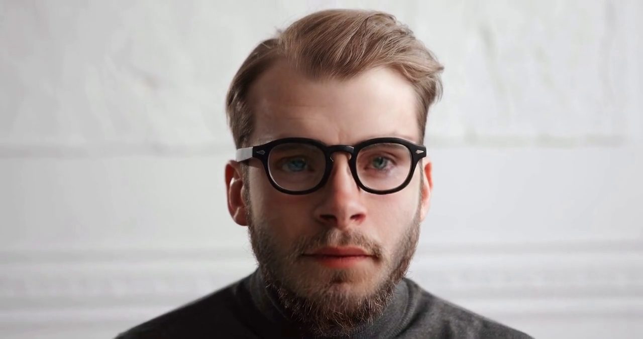 A close-up of a face with a hand in front of it and glasses on, from a video face swap test