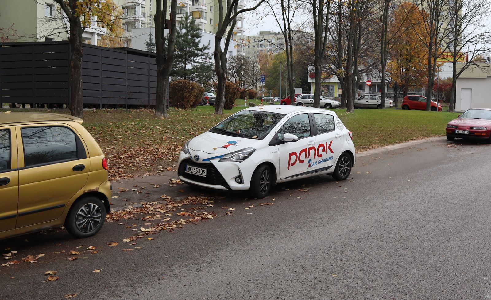 A street with parked cars before and after removing the grey hatchback with AI, the road and grass filled in and the other cars untouched — after