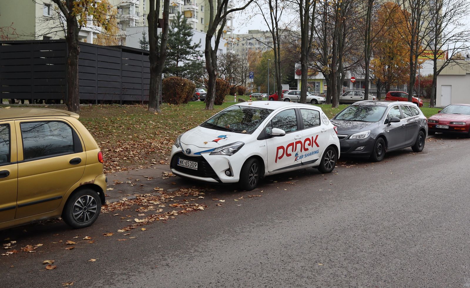 A street with parked cars before and after removing the grey hatchback with AI, the road and grass filled in and the other cars untouched — before
